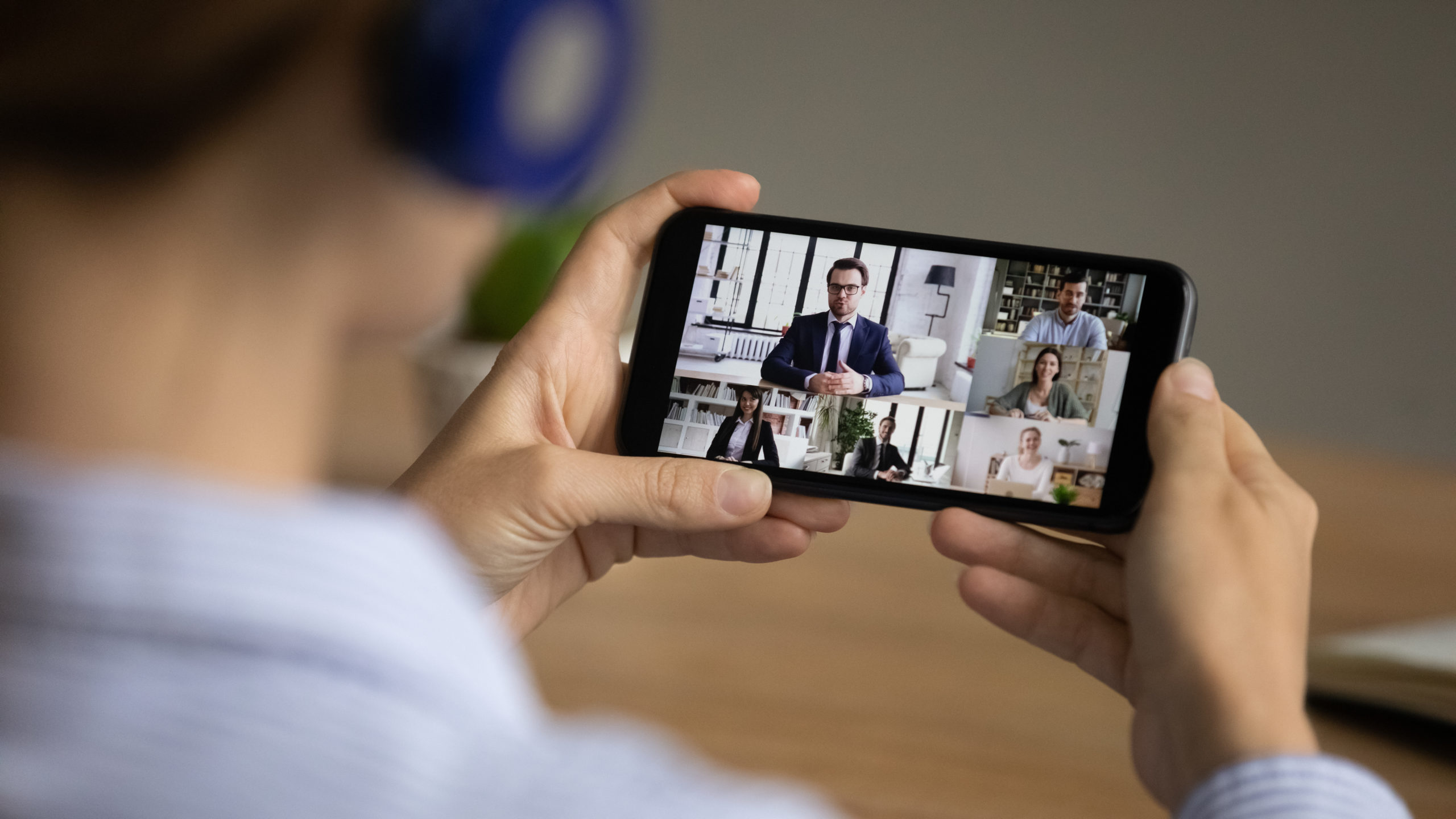 Over shoulder view of woman have online webcam digital team meeting with multiracial businesspeople on cell. Female employee talk on video call on smartphone with colleagues. Virtual event concept.